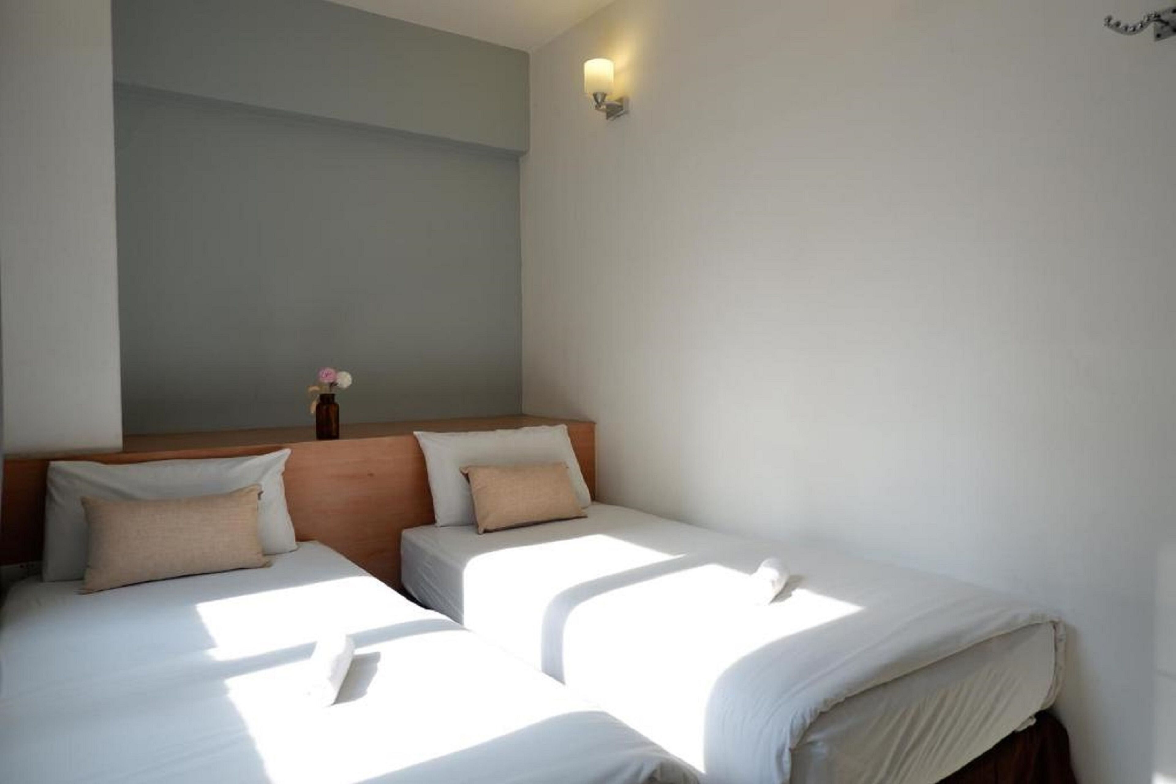 Habitación de hotel con dos camas individuales, cabecera de madera, un florero con flores y un aplique de pared.