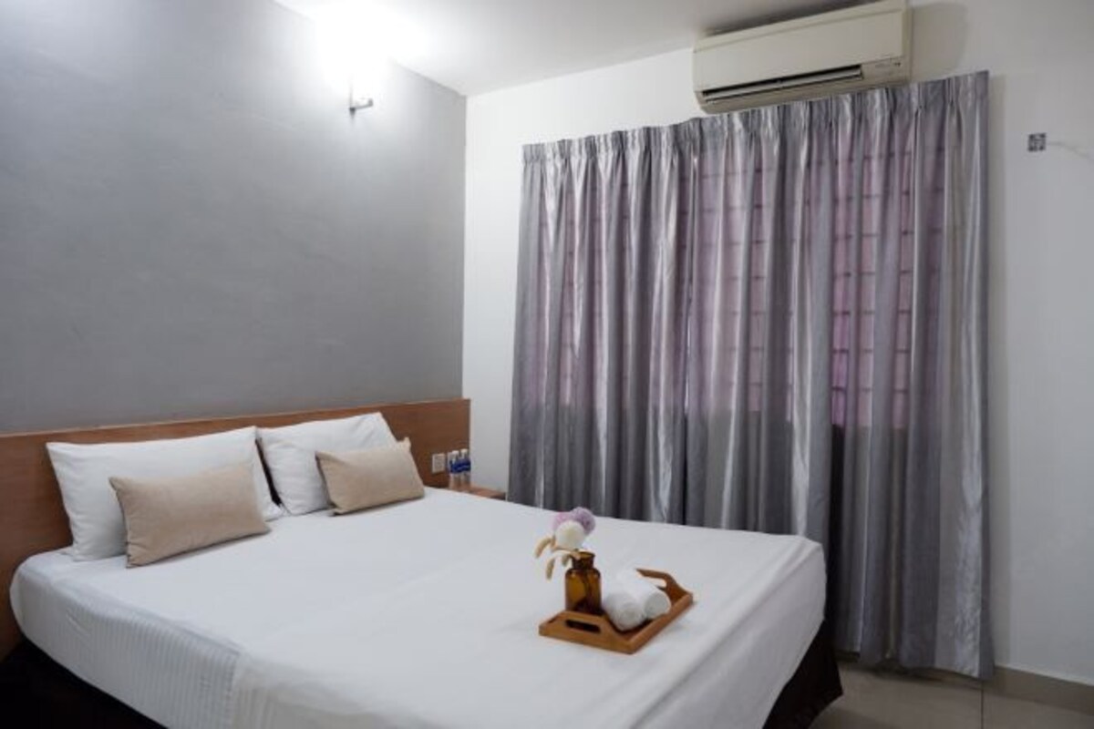 A hotel room with a bed, pillows, an air conditioner, and a curtain.