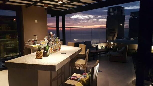 A modern kitchen with a bar area, featuring a large island with bar stools, a refrigerator, and various kitchen appliances. - Condominio Reserva del Mar, Apto Estilo Resort, Salida Privada a la Playa (Santa Marta)