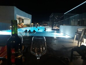A pool area with people swimming at night, a bottle of Don Slim wine, and a glass on a table. - Condominio Reserva del Mar, Apto Estilo Resort, Salida Privada a la Playa (Santa Marta)