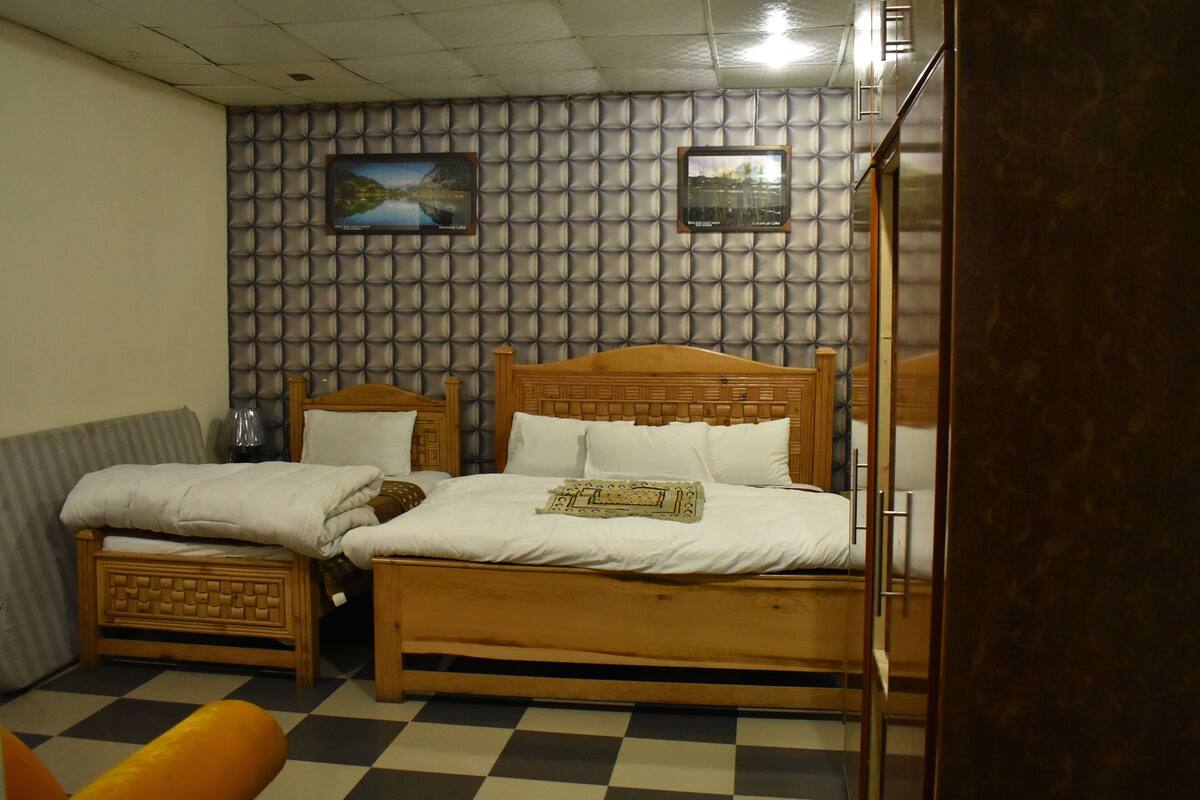A room with a checkered floor, two wooden beds, a sofa, and a wall with a patterned design.