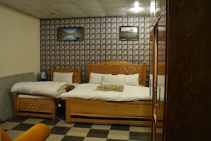 A room with a checkered floor, two wooden beds, a sofa, and a wall with a patterned design. - Rose Valley Hotel (Balakot)