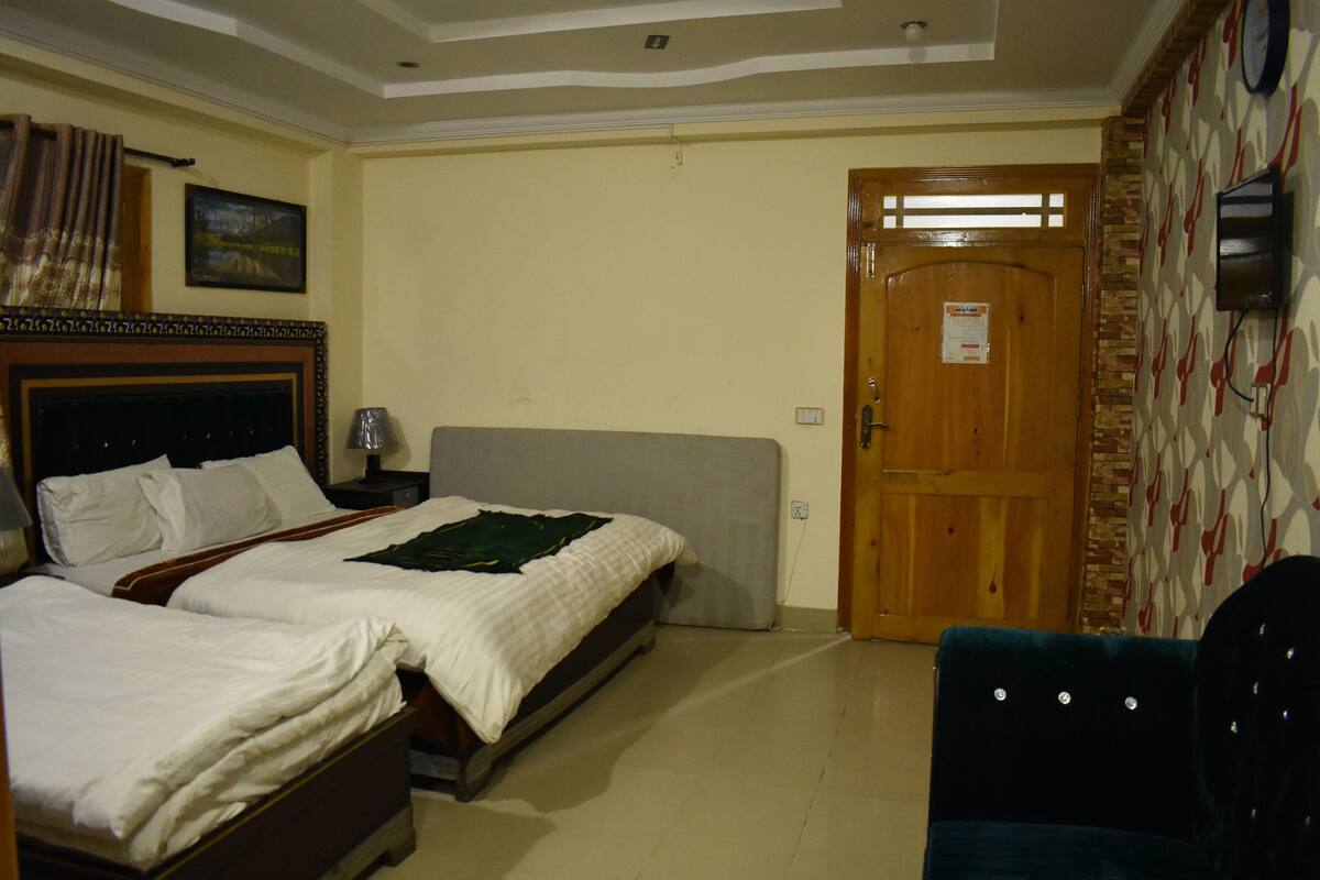 A hotel room with two beds, a wooden door, a patterned wall, and a clock.