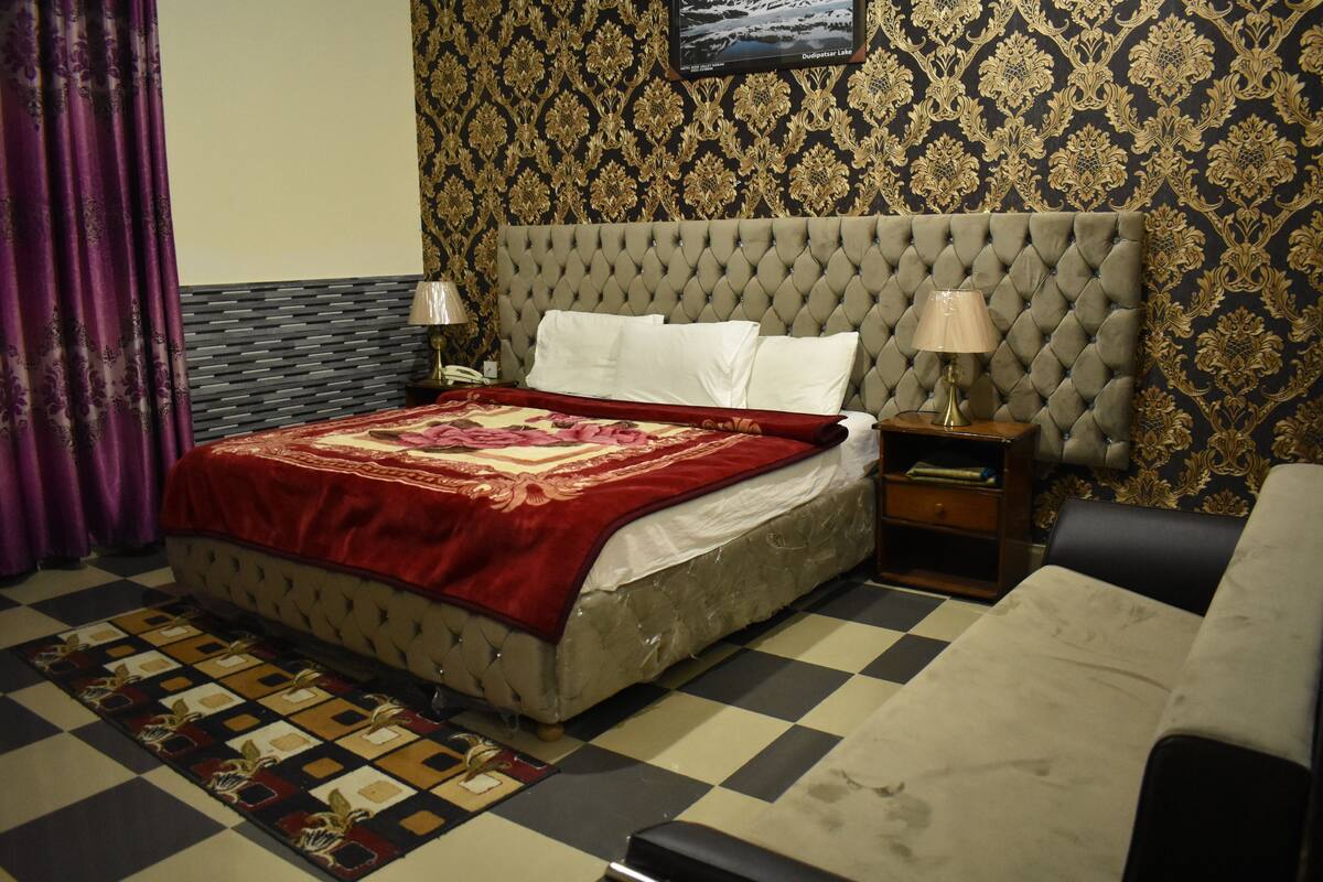 A bedroom with a tufted headboard, a checkered floor, a patterned wall, and a bed with a red and white bedspread.