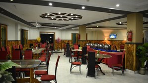 A restaurant with multiple tables and chairs, a television screen, and a fire extinguisher on the wall. - Rose Valley Hotel (Balakot)