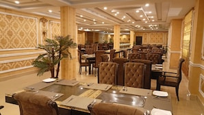 Een ruim restaurant met meerdere eettafels en stoelen, een elegante inrichting en een kroonluchter.