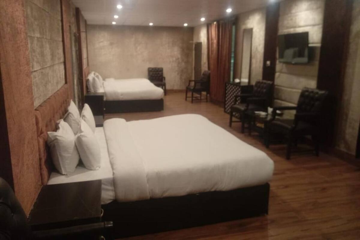 Een hotelkamer met twee bedden, een zithoek met stoelen en een aan de muur bevestigde televisie.