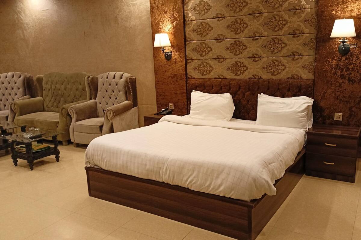 Een hotelkamer met een groot bed, twee fauteuils, een kleine tafel en twee wandlampen.