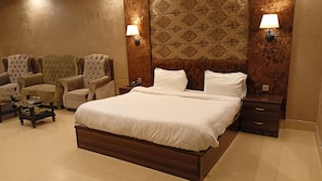 Quarto de hotel com uma cama grande, duas poltronas, uma mesinha e duas luminárias fixadas na parede.