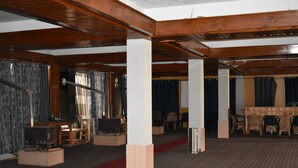 Quarto amplo com vigas de madeira, tapete vermelho e área de estar com mesas e cadeiras.