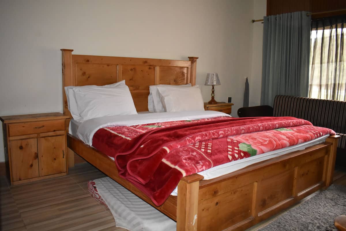 A wooden bed with white linens and a red patterned blanket, a wooden nightstand, and a lamp.