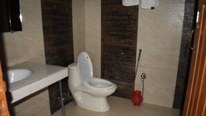 Casa de banho com sanita, lavatório e um desentupidor vermelho.