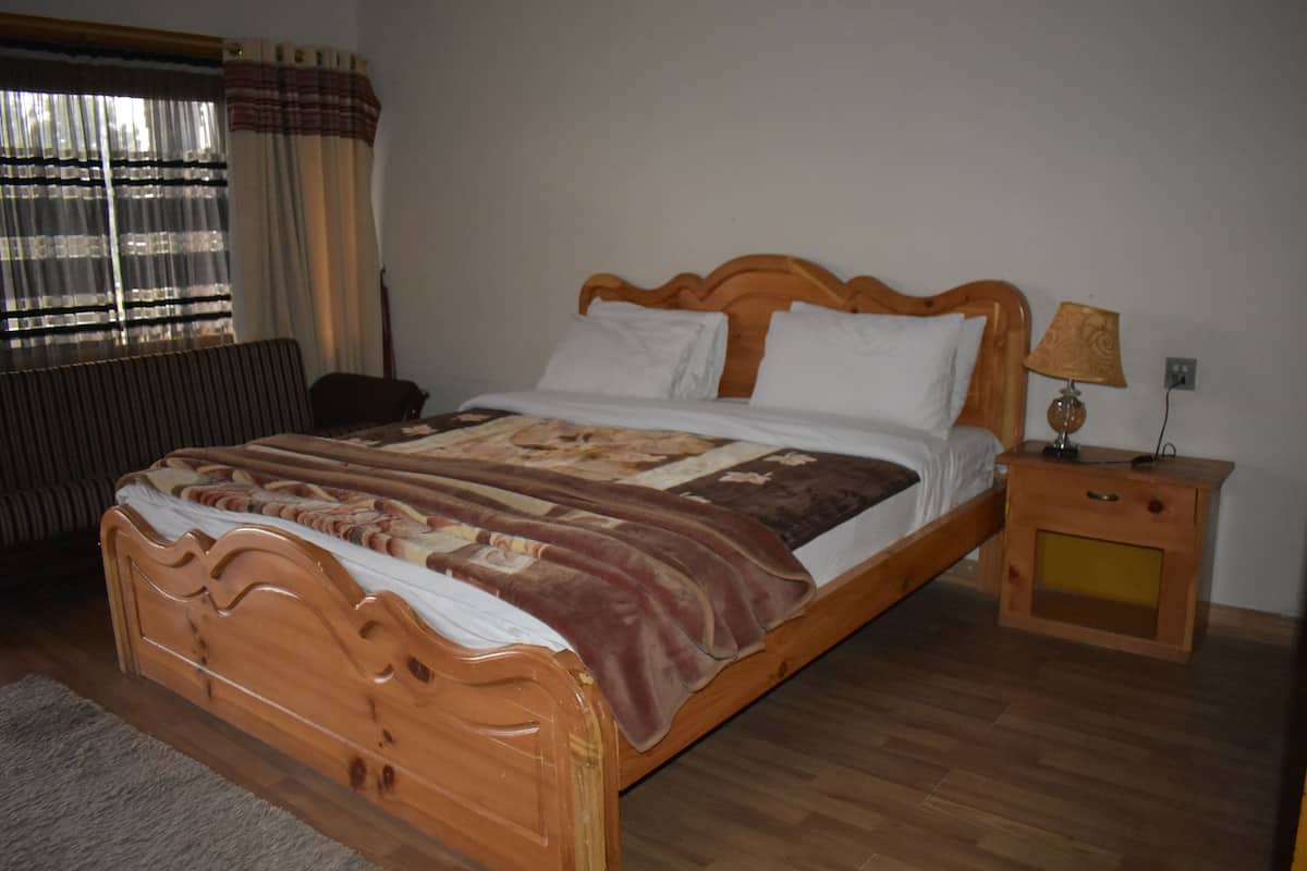 A wooden bed with a quilt, a bedside table with a lamp, and a window with curtains.