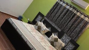 A bedroom with a bed, a green accent wall, a wall-mounted air conditioner, and patterned curtains. - Hotel Executive Lodge (Karachi)