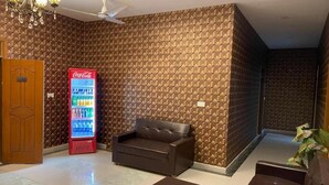 A room with a patterned wall, a sofa, a coffee table, a recliner, a door, and a Coca-Cola refrigerator. - Hotel Executive Lodge (Karachi)