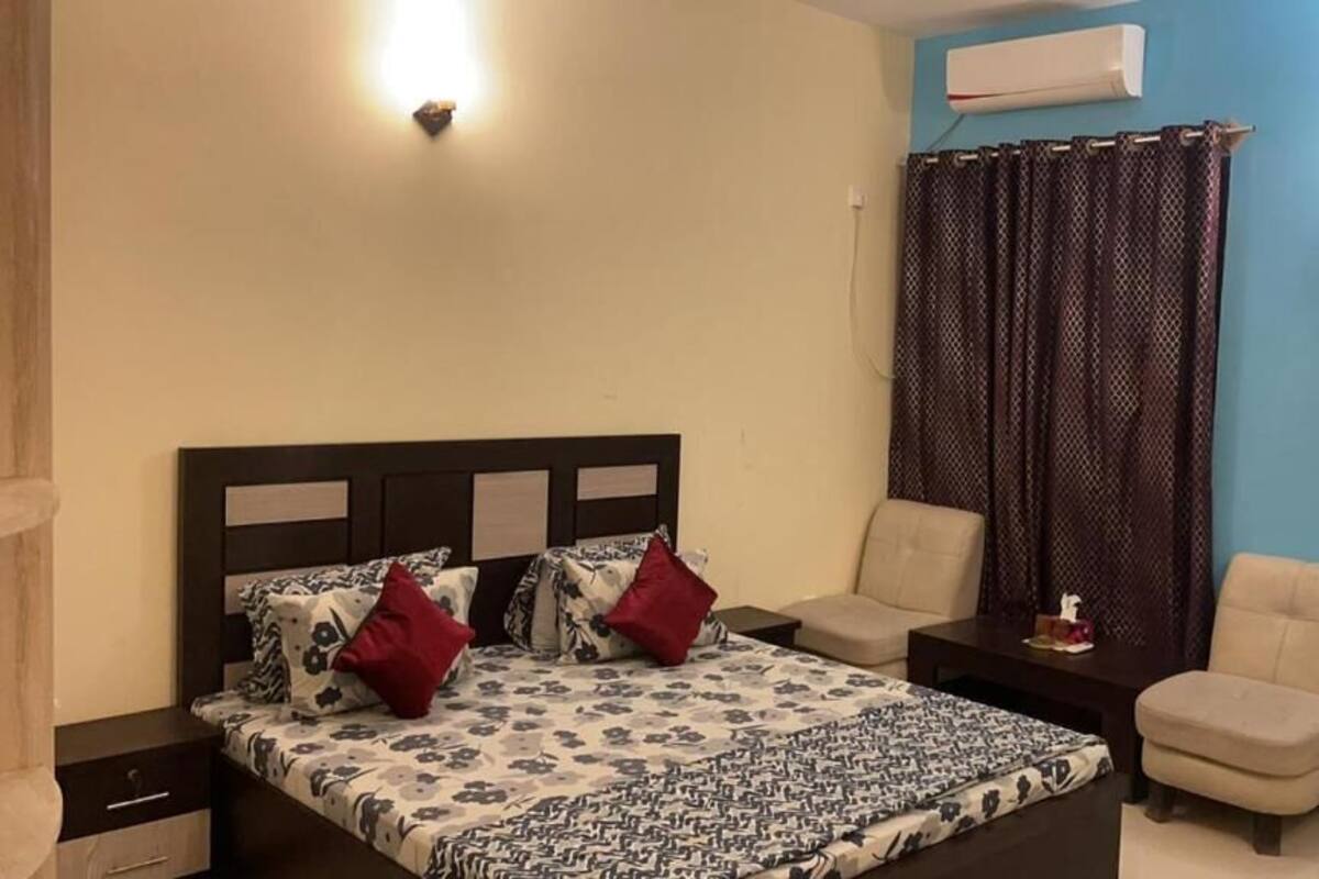 A bedroom with a bed, two chairs, a nightstand, and an air conditioning unit.