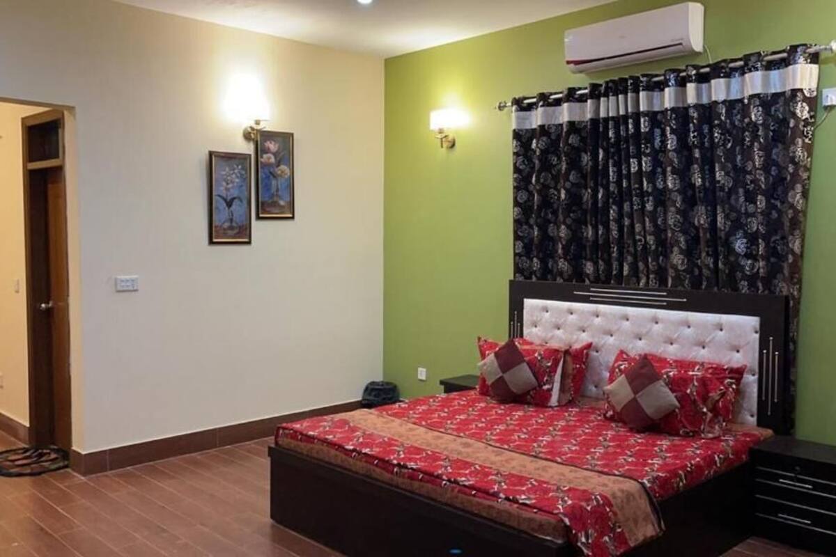 A bedroom with a bed, a nightstand, a wall-mounted air conditioner, and a door.