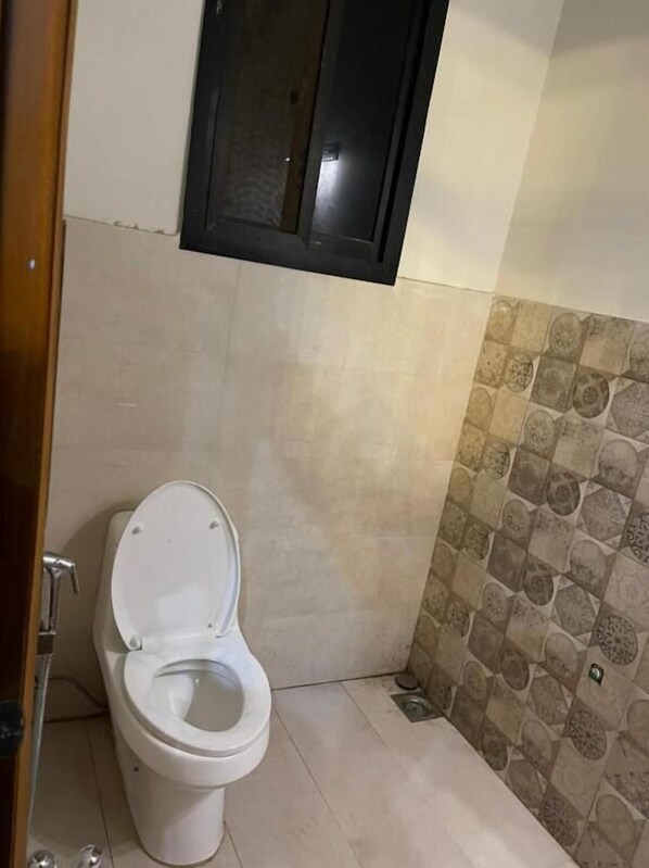 Un baño con inodoro, zona de ducha y pared de azulejos.