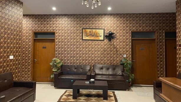 A lobby with a patterned wall, two wooden doors, a black leather sofa, a coffee table, and a chandelier. - Hotel Executive Lodge (Karachi)