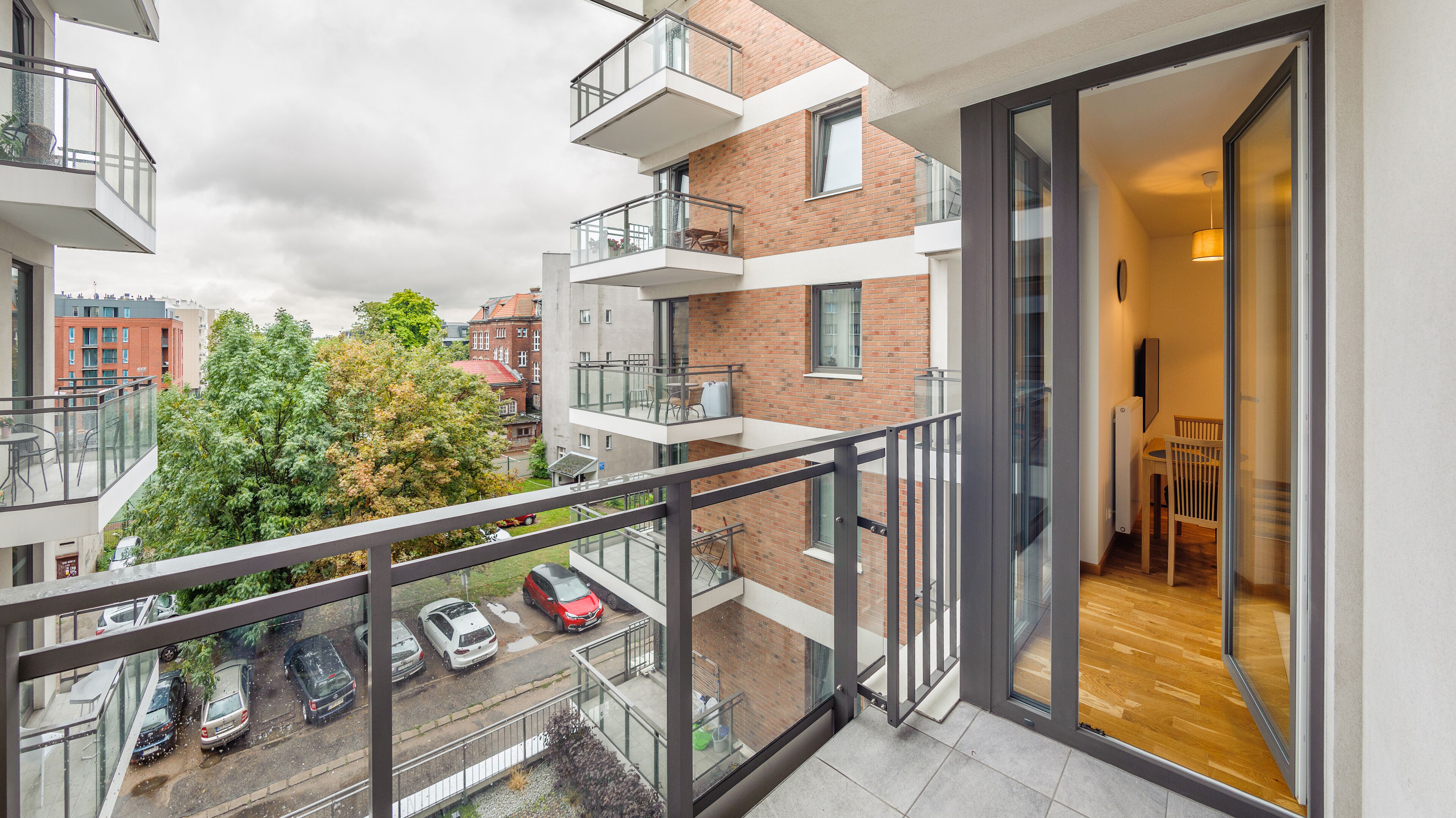 En moderne lejlighed med balkon med udsigt over en parkeringsplads og et træ.