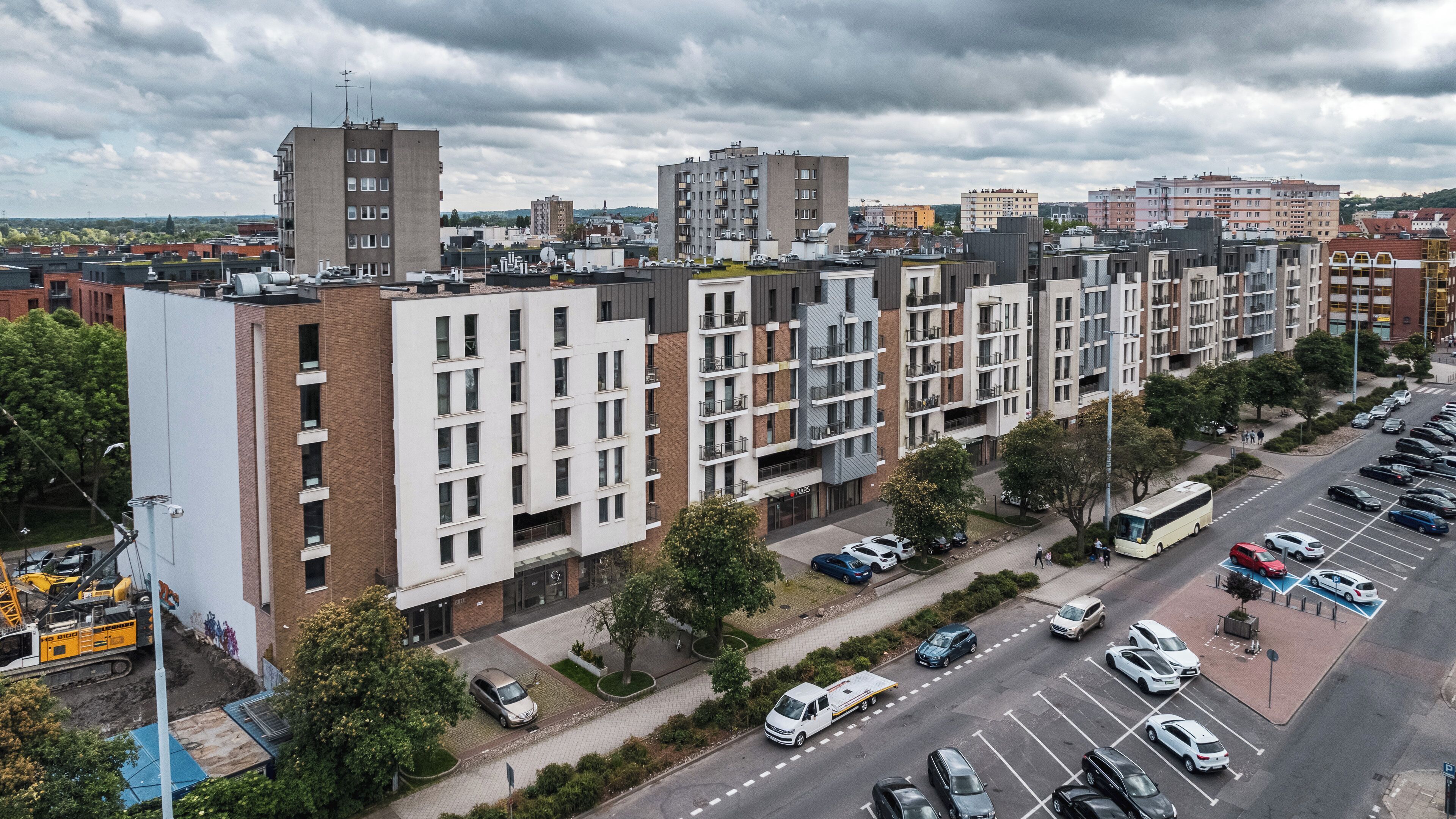 A multi-story residential building with a parking lot and a bus stop.