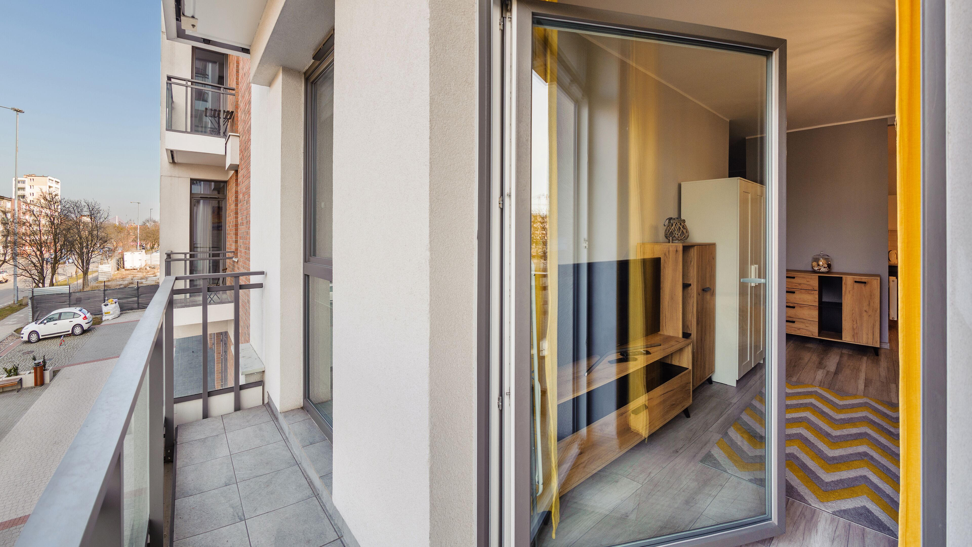 A modern apartment with a balcony, a sliding glass door leading to a living area, and a view of the street.