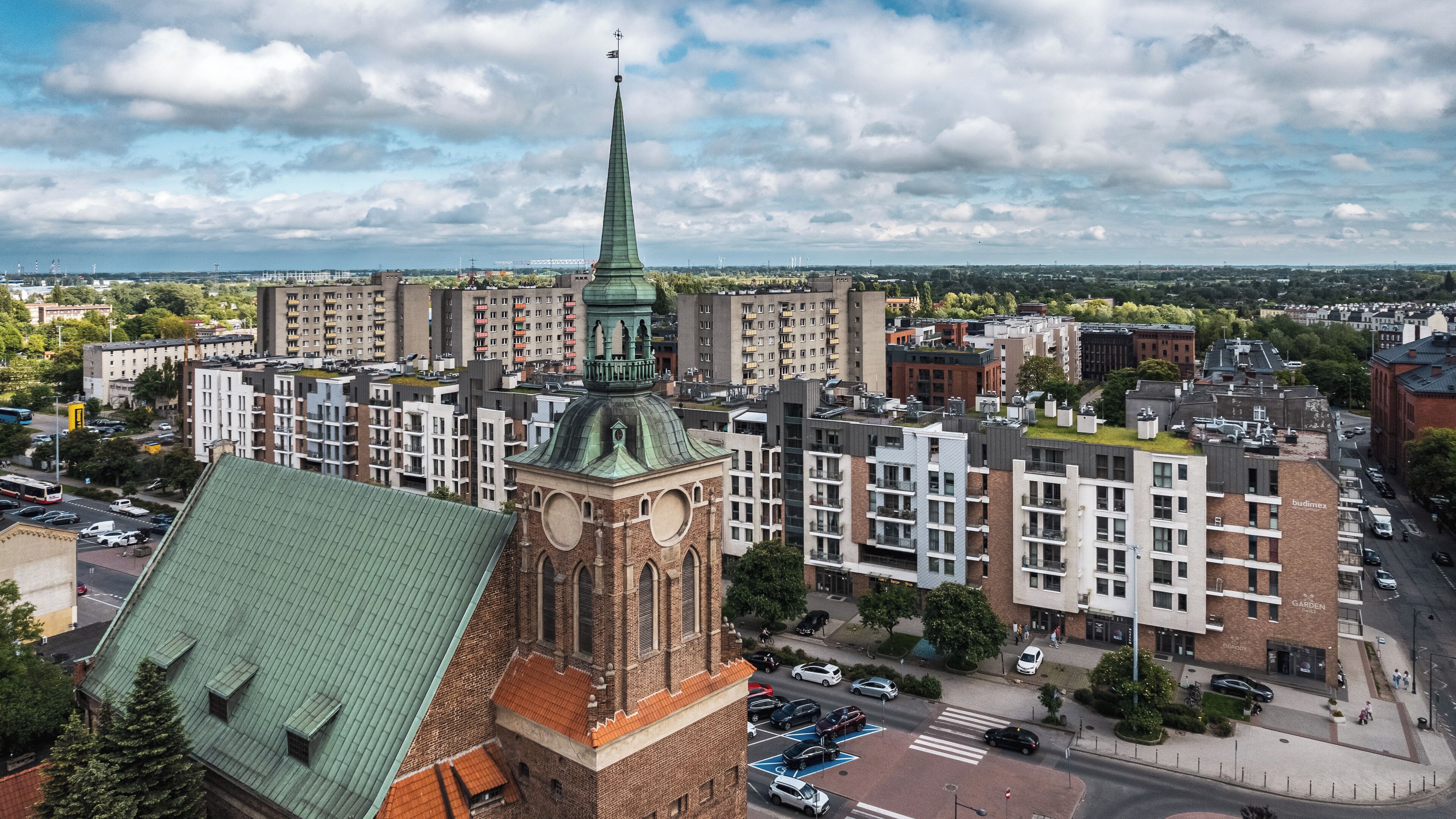 A historic building with a prominent tower and clock, surrounded by modern residential buildings and a clear sky.