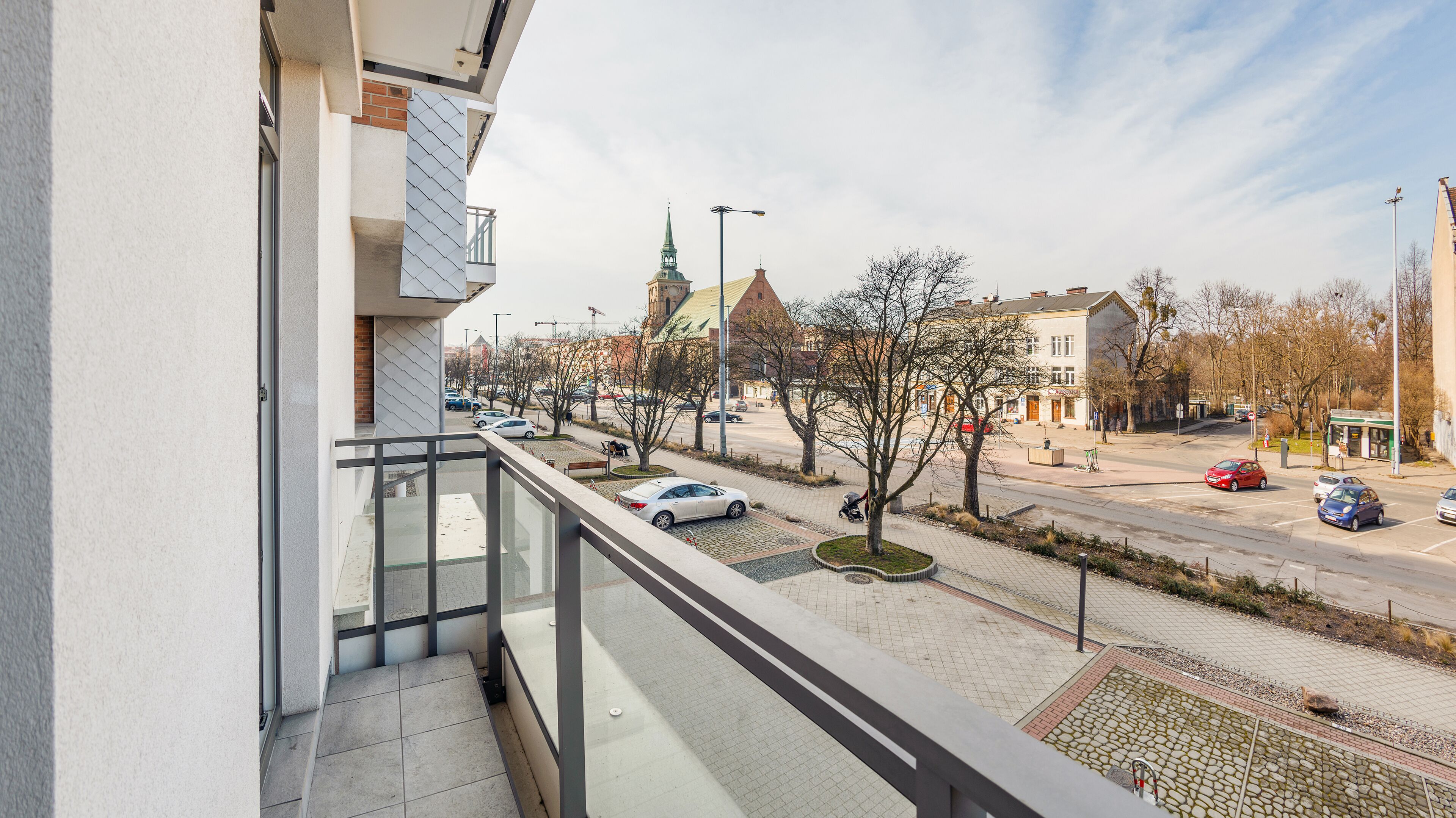 A balcony with a view of a street, cars, and buildings including a church with a green spire.