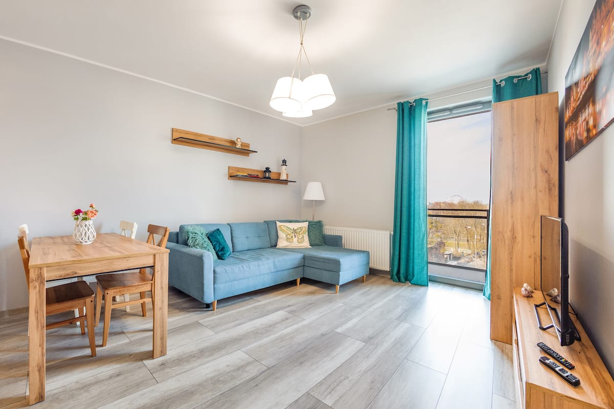 Una sala de estar moderna con una mesa de comedor de madera, un sofá azul y vistas a la ciudad a través de un ventanal grande.