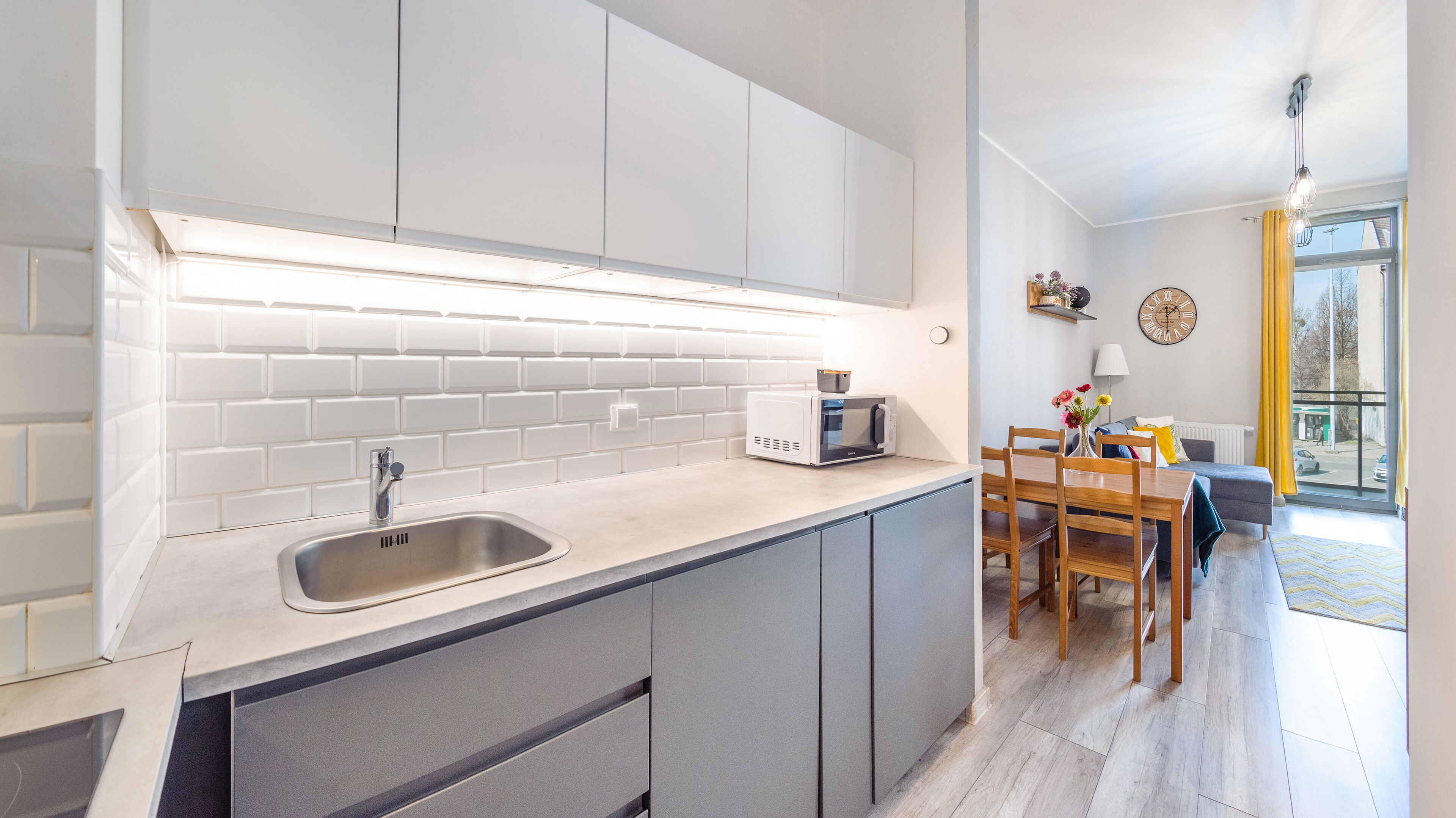 A modern kitchen with a built-in microwave, a sink, and a dining area with a table and chairs.
