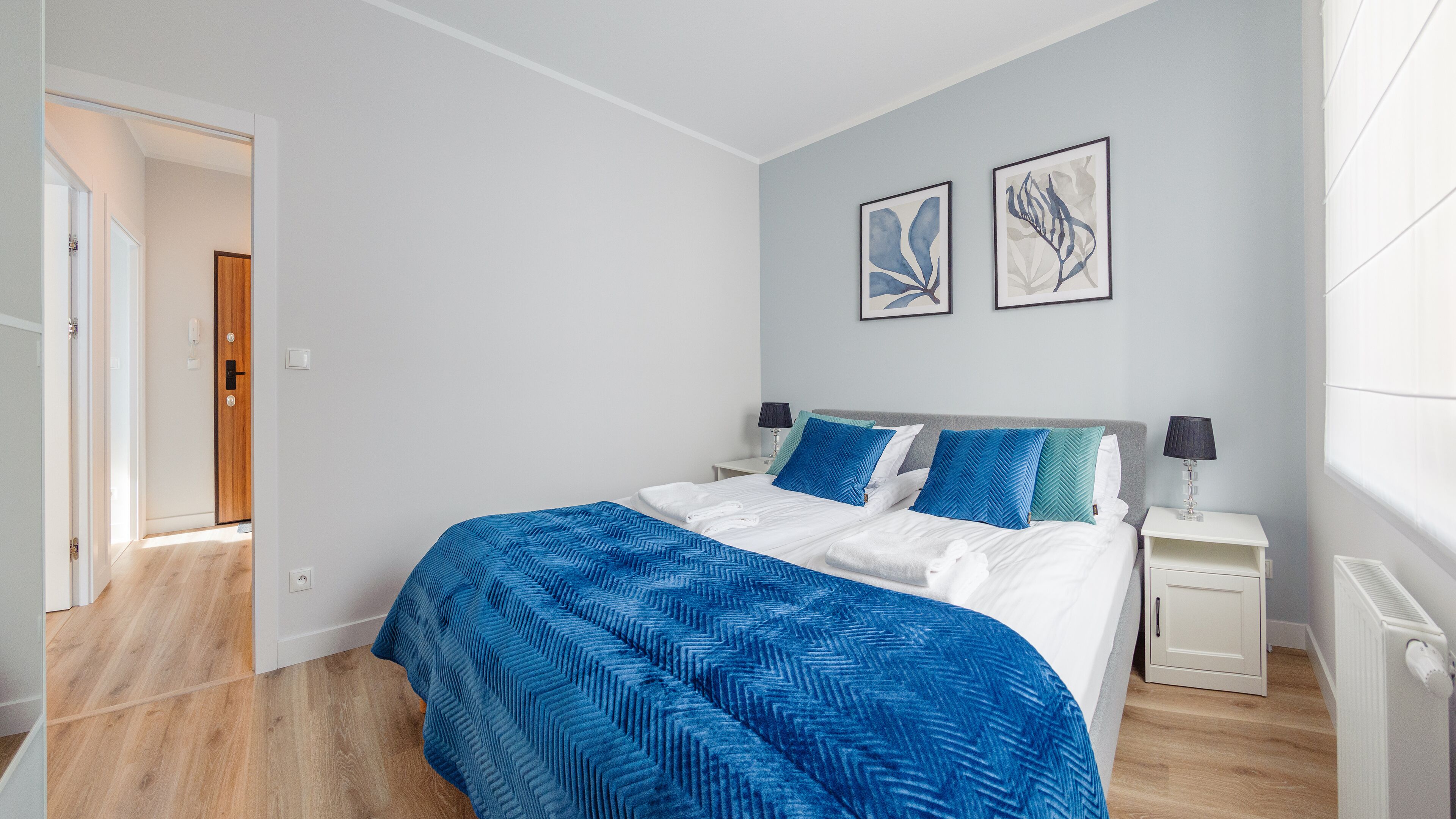 Une chambre à coucher comprenant un lit, des tables de chevet, une porte et deux œuvres d’art accrochées au mur.