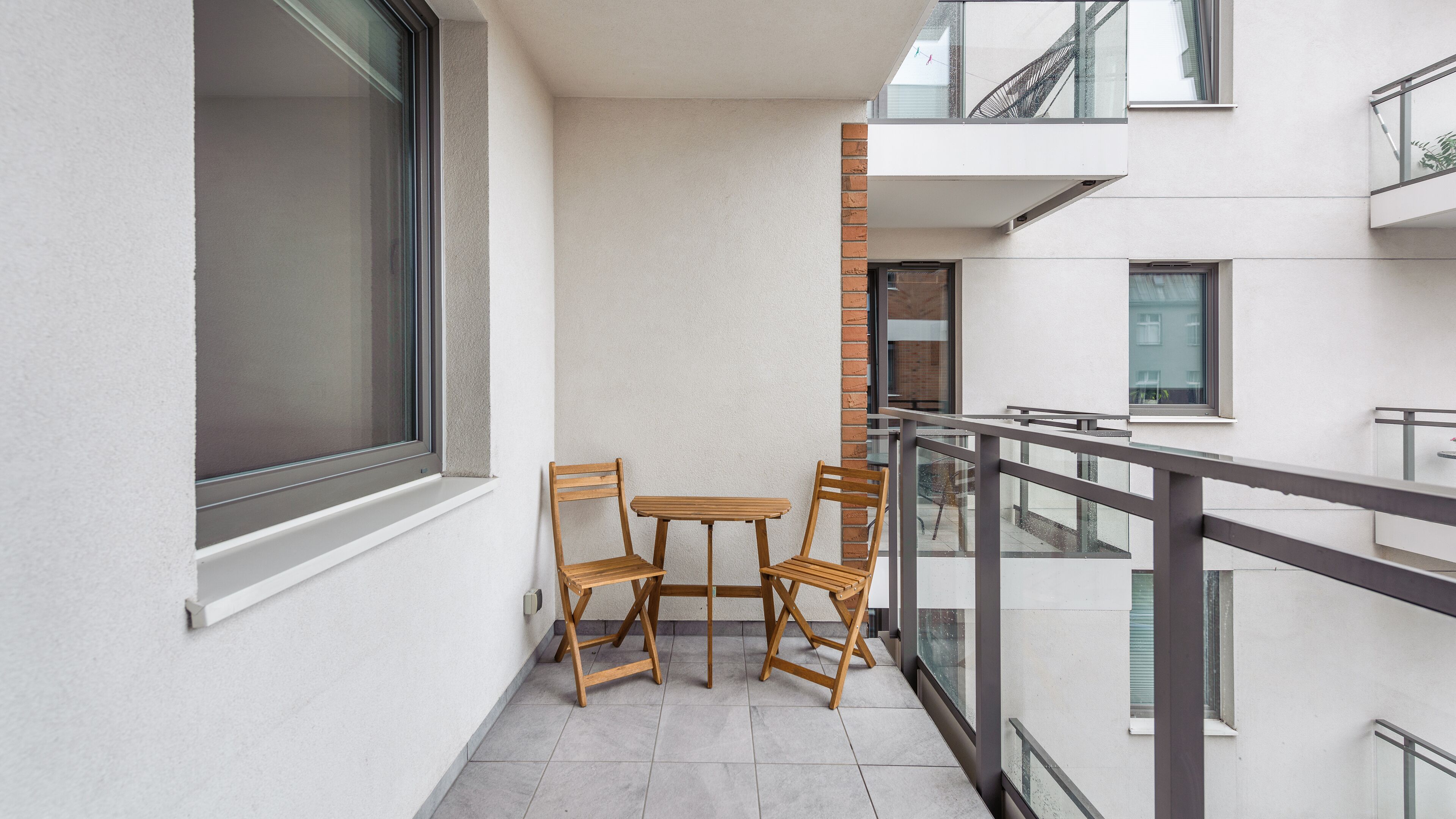 A balcony with a table and two chairs, a window, and a view of a building.