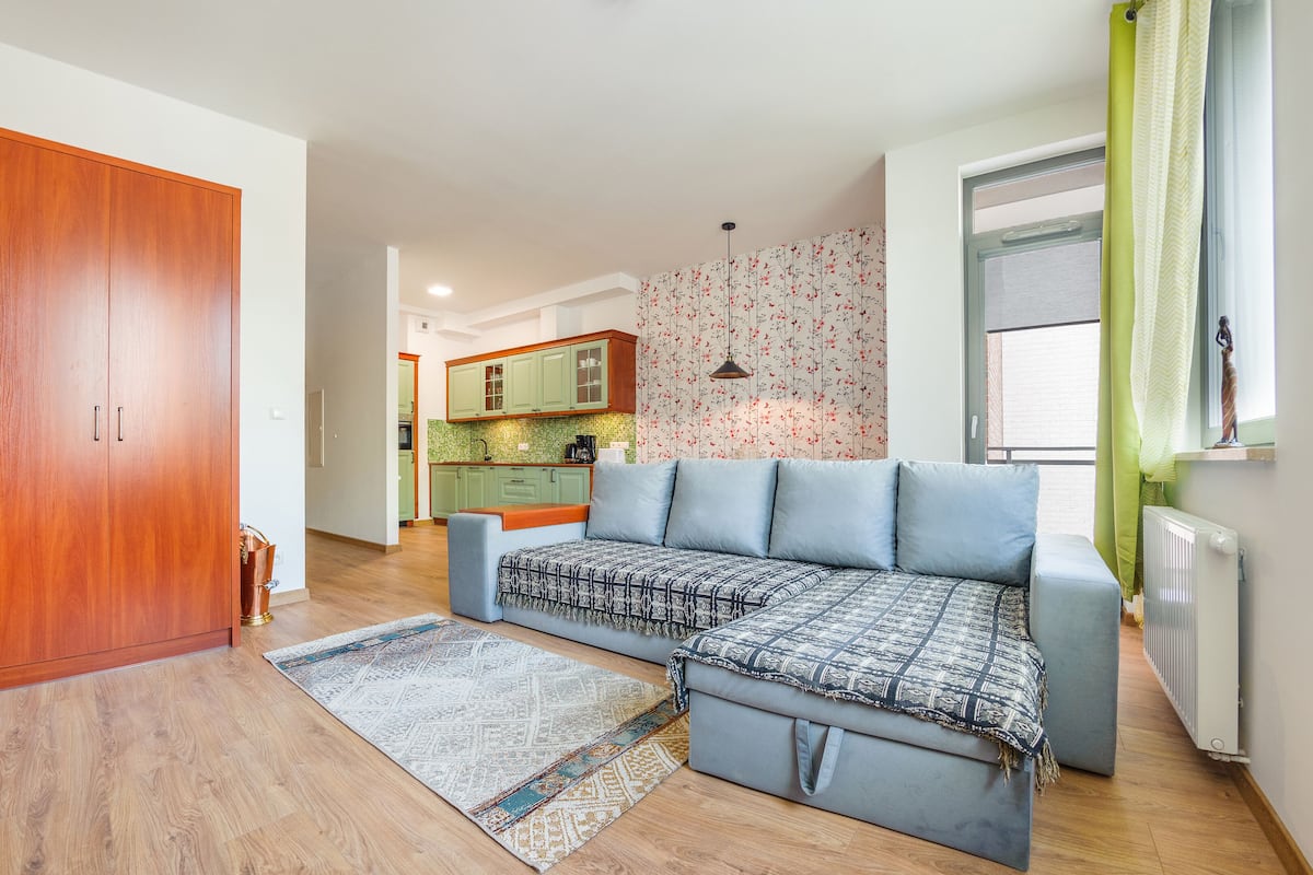 Una sala de estar moderna con un sofá modular, un armario de madera y una cocina al fondo.