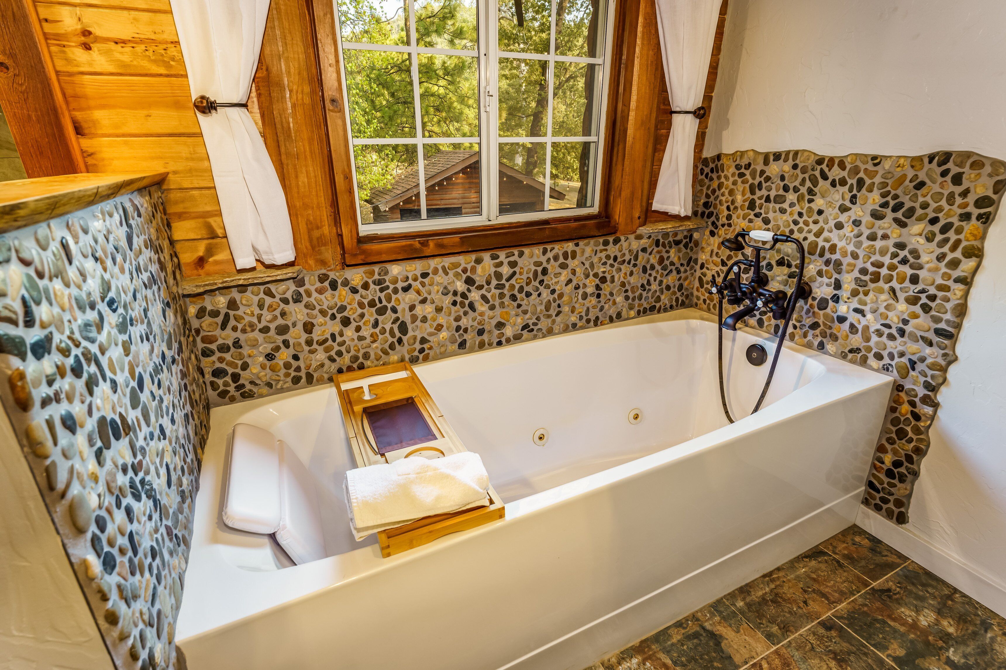 A bathroom with a stone mosaic wall, a wooden door, and a window with curtains.