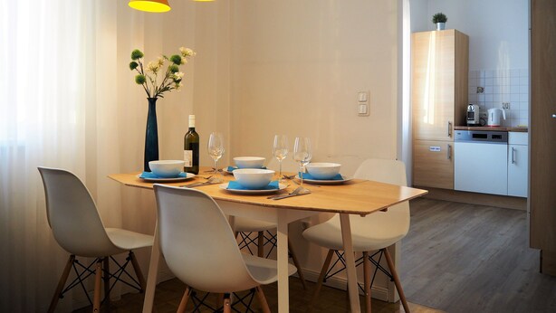 A dining area with a wooden table set for four, white chairs, and a vase with flowers. - Anastacia Premium Apartment (Graz)