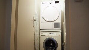 A compact, white laundry room with a front-loading washing machine, a dryer, and a small ironing board. - Anastacia Premium Apartment (Graz)