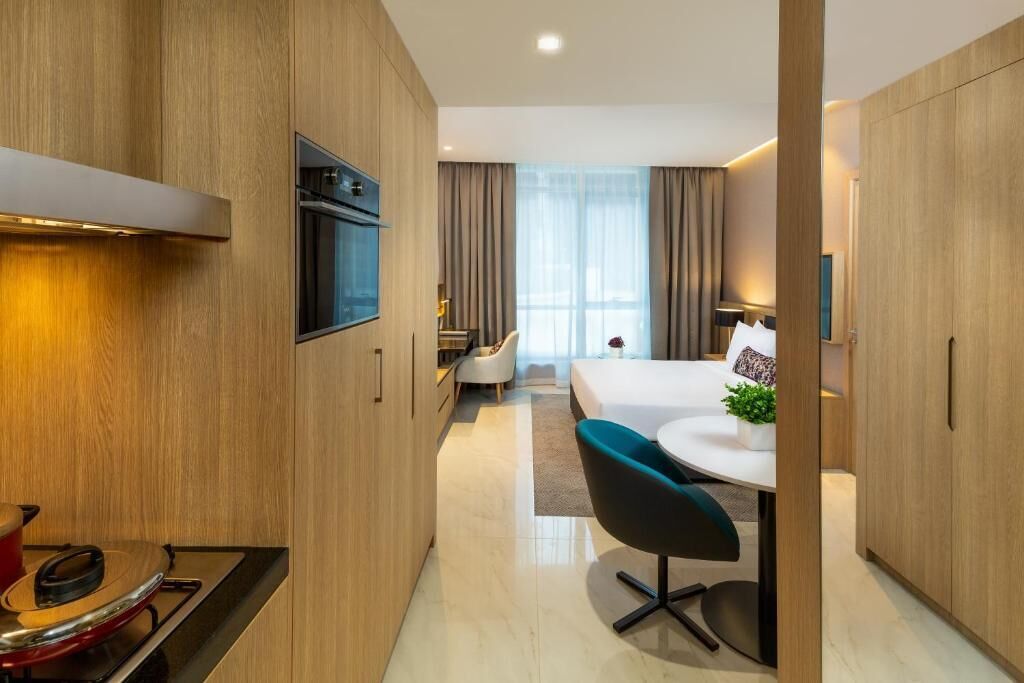 Quarto de hotel moderno com cozinha, mesa de jantar e cadeiras, cama e uma grande janela com cortinas.