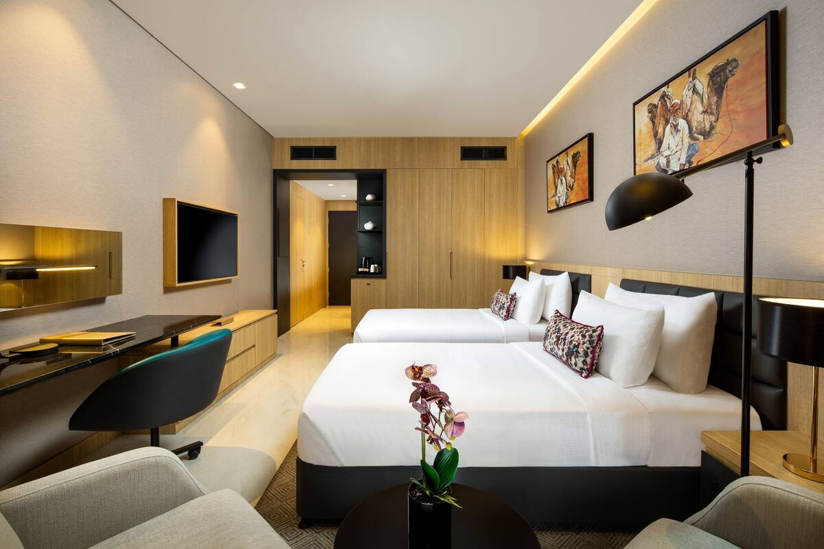 Ett modernt hotellrum med en stor säng, ett skrivbord och en stol. Det hänger en tavla på väggen och på sängen står en vas med blommor.