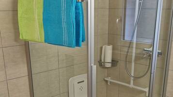 A glass-enclosed shower stall with a towel rack holding two towels, a hand dryer, and a paper towel dispenser.