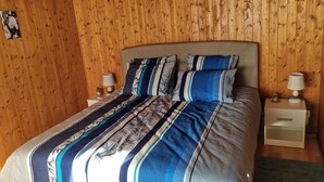 A bed with a patterned bedspread, two bedside tables with lamps, and a wooden wall. - Chez Rosalie (La Roche FR)
