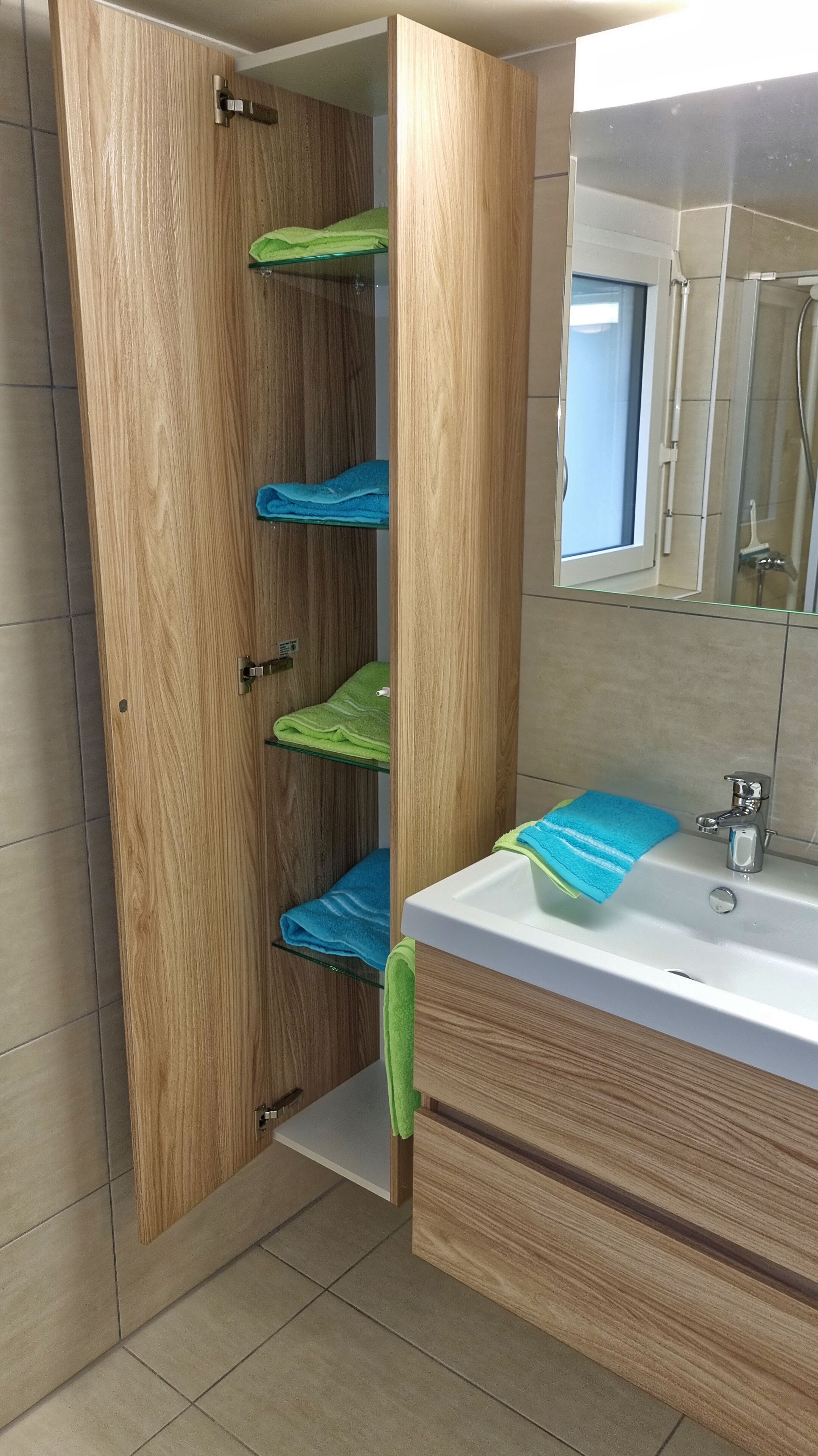 Een badkamer met een houten wastafelmeubel, een wastafel en een spiegel. Er zijn verschillende planken met handdoeken.