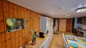 A kitchen with wooden walls, a checkered floor, a dining table with colorful plates, and a coffee machine. - Chez Rosalie (La Roche FR)