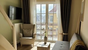 Una sala de estar con sofá, sillón, mesita, televisor y ventana grande con cortinas.