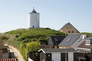 Un bâtiment situé sur la côte, doté d’un château d’eau, d’un sentier menant vers le haut d’une colline et d’une maison avec un toit en pente.