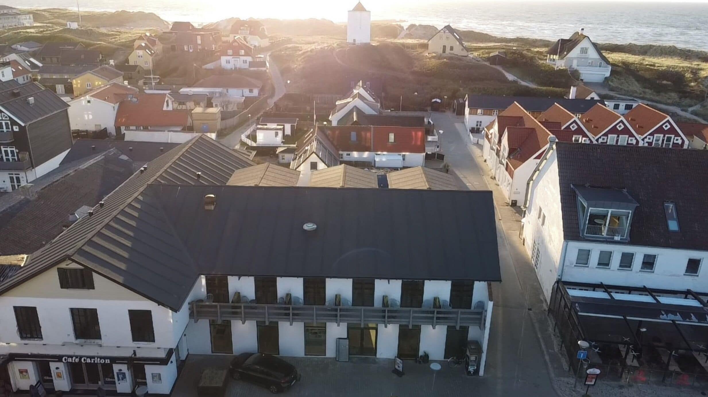 Luchtbeeld van een kustplaats met gebouwen, waaronder een café genaamd 'Café Carlton'.