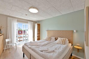 Une chambre d’hôtel moderne avec un grand lit, une tête de lit en bois, une petite table et une vue sur l’extérieur.