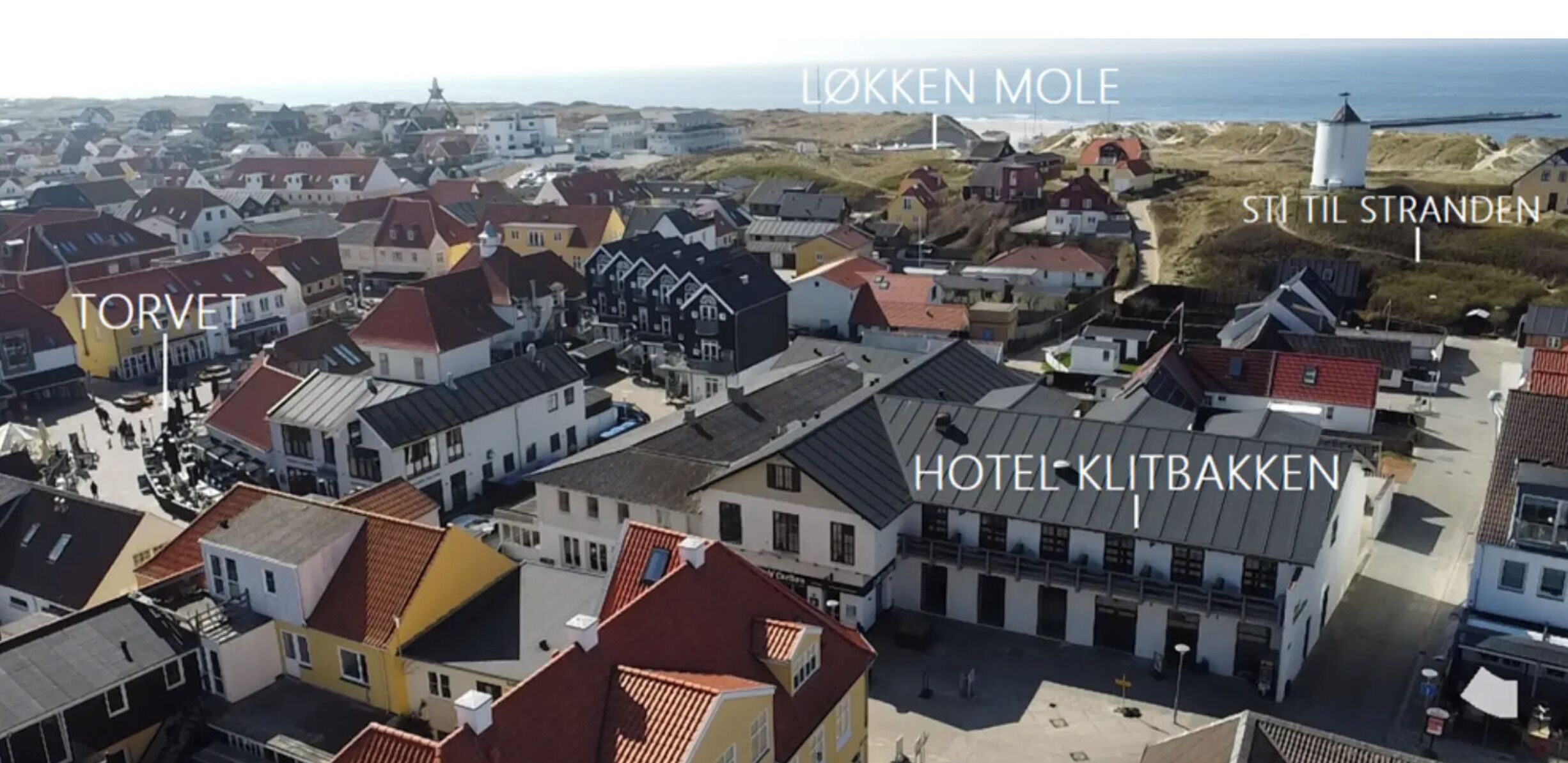 Une ville côtière où l’on peut voir des bâtiments portant les inscriptions « LØKKEN MOLE » et « STIL TIL STRANDEN ».
