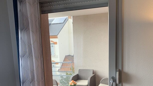 Eine Glastür führt zu einem Außenbereich mit Korbmöbeln und einem kleinen Tisch mit Blumen.