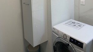 Ein Waschbereich mit einer weißen Waschmaschine, einem Schrank und einem an der Wand befestigten Diffusor mit Rattan-Duftstäbchen.