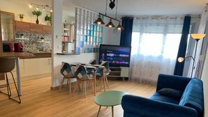 Ein modernes Wohnzimmer mit einem blauen Sofa, einem Essbereich mit einem grünen Tisch und einer Küche mit Holzschränken und einer gefliesten Spritzschutzwand.